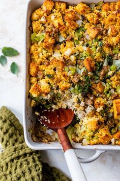 a casserole dish filled with stuffing and vegetables next to a green mitt