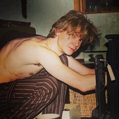 a shirtless man leaning over a table with a coffee cup in front of him