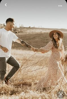 a man and woman holding hands while walking through tall grass in an open field together