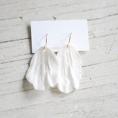 two pairs of white leather earrings on top of a piece of paper next to a business card