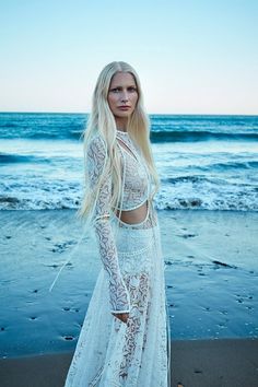 a woman standing on top of a sandy beach next to the ocean wearing a white dress