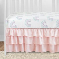 a baby crib bed with pink ruffled bedspread and rainbows on it