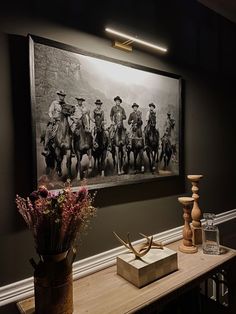 an old photo hangs on the wall above a table with vases and flowers in front of it