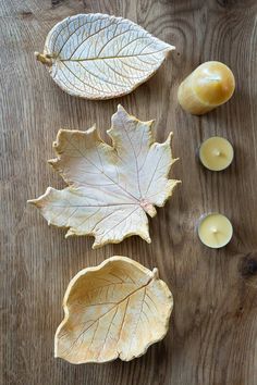 three leaves and two candles on a wooden table with one candle in the middle next to it