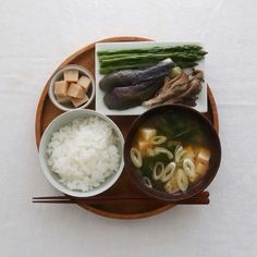 a wooden plate topped with rice, meat and veggies next to chopsticks