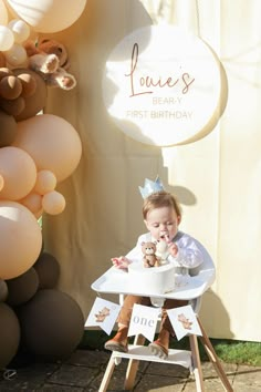 a baby sitting in a high chair next to balloons and a sign that says love's beary first birthday