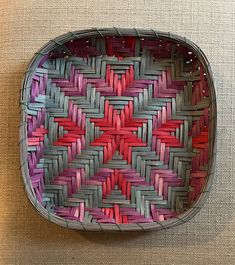 a woven basket with red, pink and blue strips in it on a beige surface