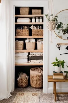 an open closet with baskets and towels on the shelves next to a table, mirror and rug