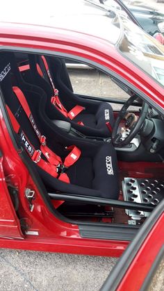 the interior of a red sports car with its door open and steering wheel still in place