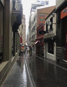 an empty city street in the rain with buildings and shops on either side as people walk down the sidewalk