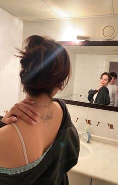 a woman with a tattoo on her back standing in front of a mirror