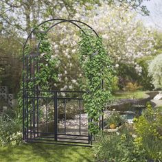 an iron garden trellis in the middle of a yard with flowers and trees around it