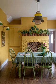 a dining room table with green chairs and a blue table cloth on it, in front of a yellow brick fireplace