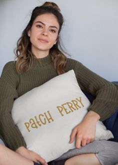 a woman sitting on a couch holding a pillow with the words patch perry printed on it