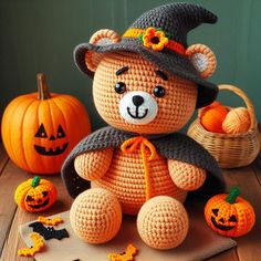 a crocheted teddy bear wearing a witches hat and sitting on a table with pumpkins