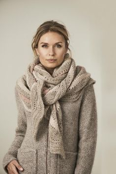 a woman wearing a gray sweater and scarf standing in front of a white wall with her hands on her hips