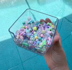 a hand holding a container filled with lots of small beads next to a swimming pool