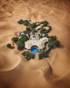 an aerial view of a house in the middle of sand dunes with trees around it