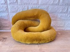 a yellow pillow sitting on top of a wooden floor next to a white brick wall