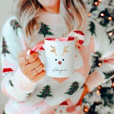 a woman holding a coffee mug in front of a christmas tree