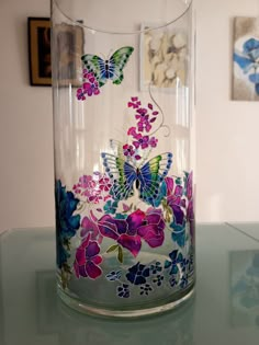 a glass vase with butterflies and flowers painted on the inside is sitting on a table