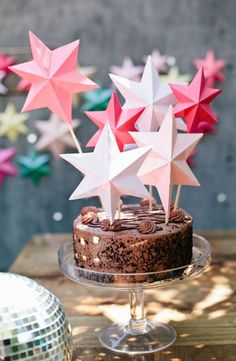 a chocolate cake topped with pink stars on top of a wooden table next to disco balls