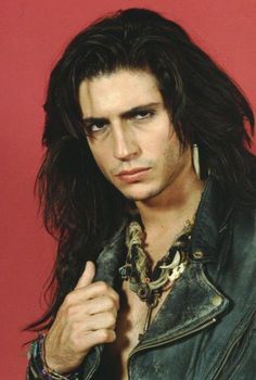 a man with long hair wearing a black leather jacket and chain around his neck is looking at the camera