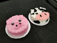 two cakes decorated to look like farm animals on top of black table cloth with pink and white frosting