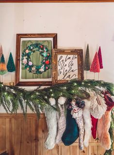 christmas stockings hanging from a mantle with holiday decorations on the mantle and framed wreaths