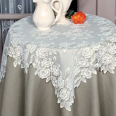 two white vases sitting on top of a table next to a flower pot and curtain