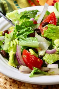 a salad with lettuce, tomatoes, onions and olives on a white plate