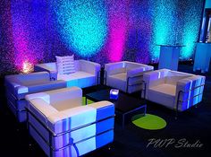 a room with couches, tables and chairs lit up by colorful lights on the walls