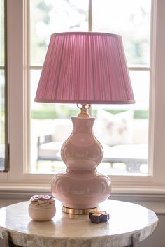 a pink lamp sitting on top of a marble table next to a window with a pink shade