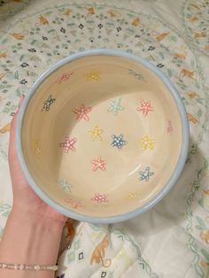 a hand holding a bowl on top of a bed next to a dog print comforter