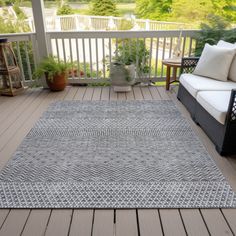 an outdoor area rug on a deck with two couches and potted plants in the background