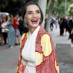 a woman in a red and yellow jacket smiles at the camera while standing on a sidewalk