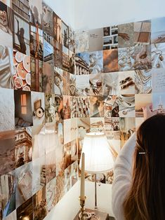 a woman sitting in front of a lamp with many pictures on the wall behind her