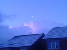 the sun is setting over some houses with clouds in the sky behind them and a half moon on the horizon