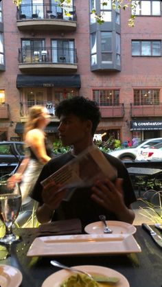 a man sitting at a table in front of a woman holding a box with food on it