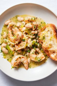 a white plate topped with shrimp and broccoli covered in sauce next to a piece of bread