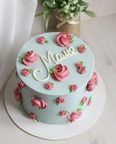 a blue cake with pink roses and the word maue on it is sitting next to a potted plant