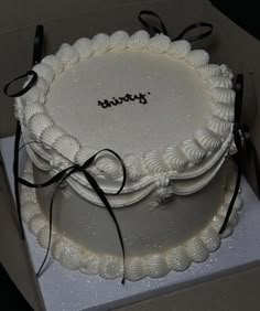 a white cake sitting on top of a box with black ribbon around the edges and writing on it