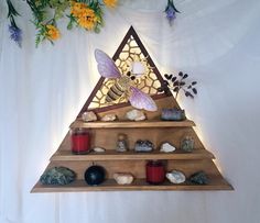 a wooden shelf with candles, rocks and a bee on it in the shape of a triangle