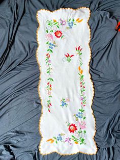 an embroidered cloth with flowers on it laying on a blue bed sheet and two red scissors