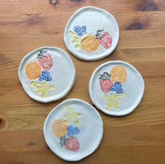 three plates with fruit painted on them sitting on a wooden table next to each other