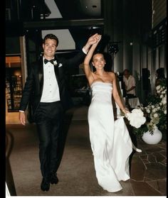 a man and woman in formal wear walking down a hall holding each other's hands