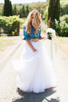 a woman in a white dress holding a bouquet of flowers on the side of a road