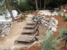 lounge chairs are lined up on the side of a beach near some trees and water