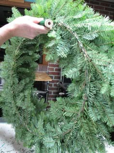 a person is holding a green wreath in front of a brick wall and building with windows