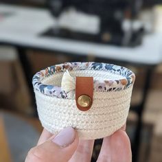 a woman holding up a white woven basket with leather button on the top and handles